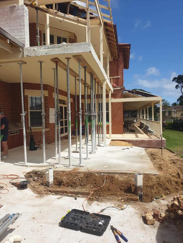 Steel props holding up a brick home's balcony while the ground below is dug out
