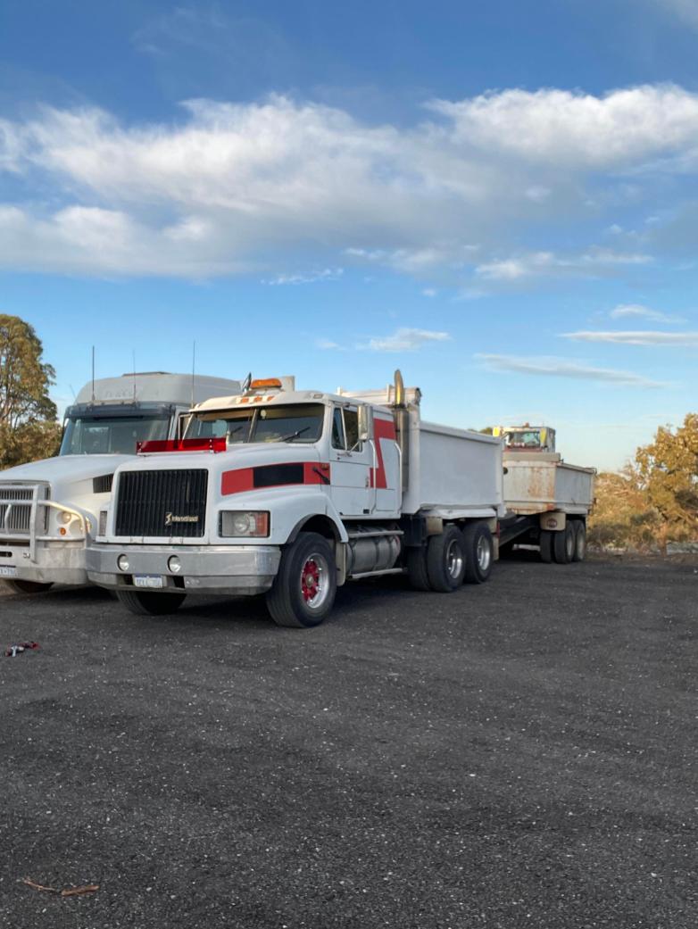 White tipper trucks with trailers parked on a gravel yard